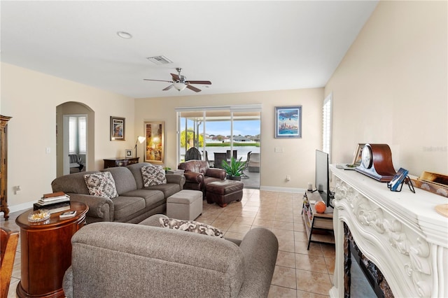 living area featuring arched walkways, light tile patterned floors, visible vents, a ceiling fan, and baseboards