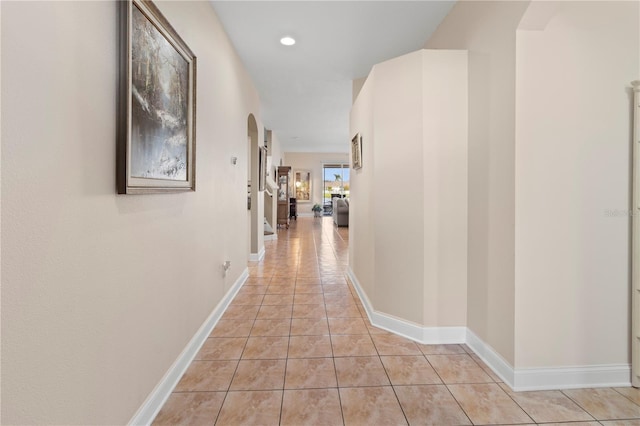 corridor with arched walkways, recessed lighting, baseboards, and light tile patterned floors