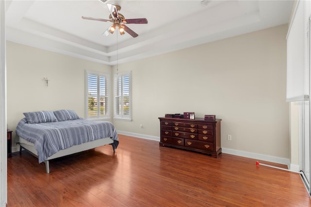 bedroom featuring wood finished floors, a raised ceiling, a ceiling fan, and baseboards