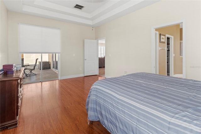 bedroom featuring a tray ceiling, visible vents, a high ceiling, and hardwood / wood-style flooring