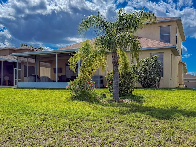 back of property featuring a sunroom, central air condition unit, a yard, and stucco siding