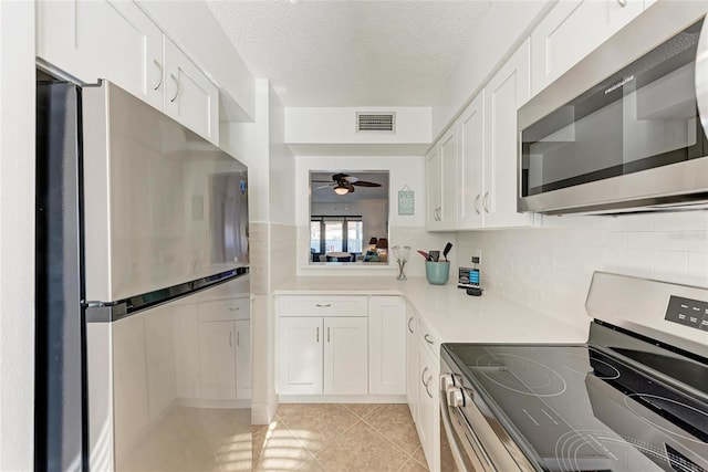 kitchen featuring light tile patterned flooring, white cabinets, ceiling fan, stainless steel appliances, and a textured ceiling