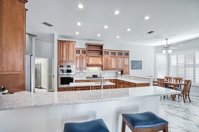 kitchen with stainless steel appliances, light stone countertops, a kitchen bar, and kitchen peninsula