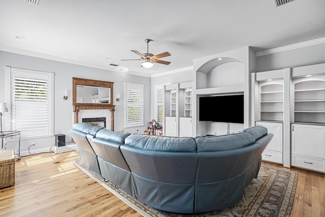 living room featuring crown molding, built in features, ceiling fan, and light wood-type flooring