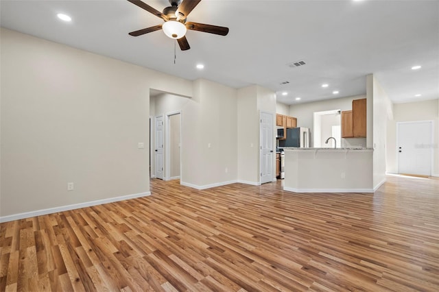 unfurnished living room featuring sink, light hardwood / wood-style flooring, and ceiling fan