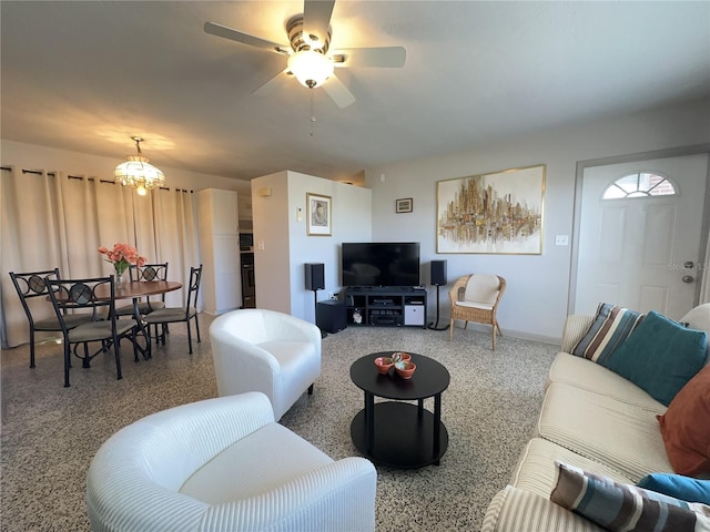 living room with ceiling fan with notable chandelier, speckled floor, and baseboards