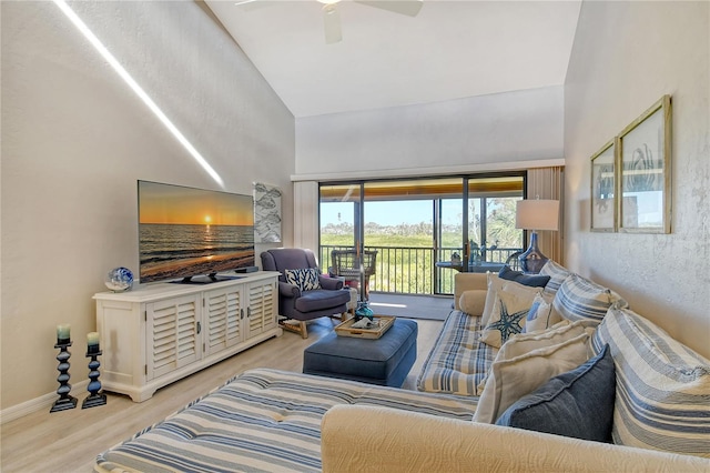 living area with high vaulted ceiling, light wood-type flooring, baseboards, and a ceiling fan