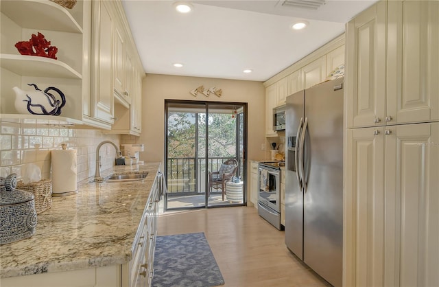 kitchen featuring cream cabinetry, stainless steel appliances, backsplash, light wood-style floors, and a sink