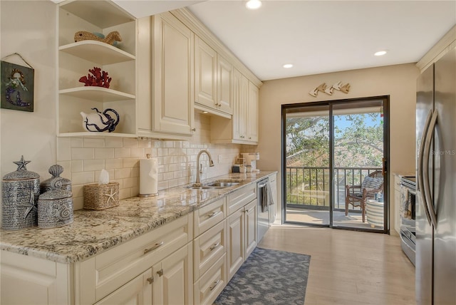 kitchen featuring stainless steel appliances, light wood-style floors, a sink, and light stone countertops