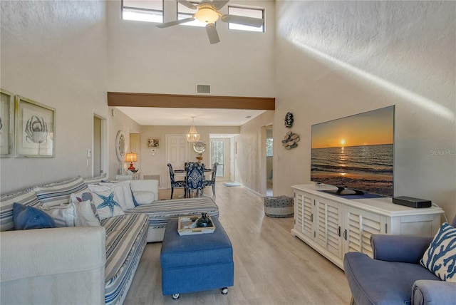 living room with a healthy amount of sunlight, light wood-style floors, a towering ceiling, and a ceiling fan