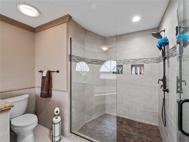 full bath featuring toilet, a wainscoted wall, a tile shower, and tile walls