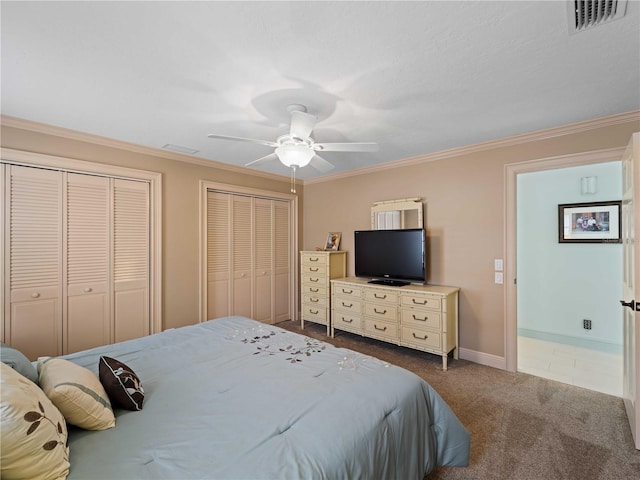 bedroom with multiple closets, dark colored carpet, visible vents, and ornamental molding