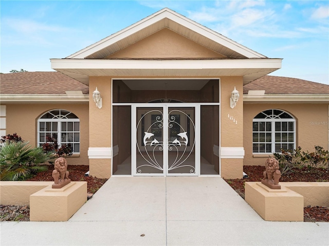 view of exterior entry with driveway, a shingled roof, a garage, and stucco siding