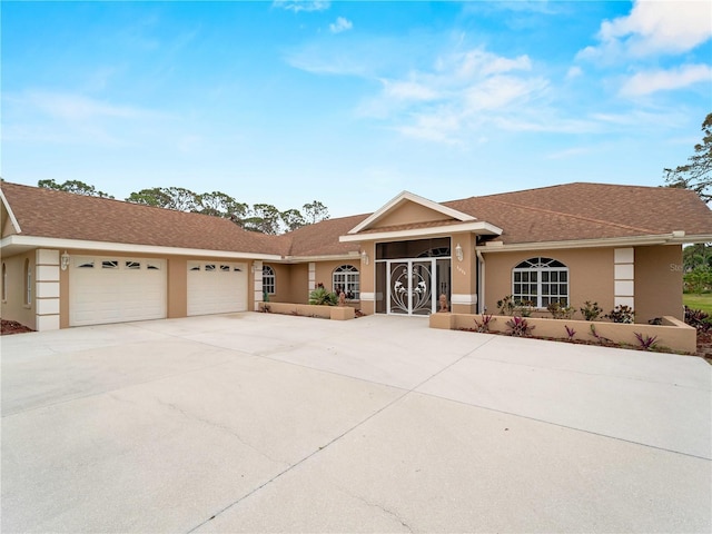 ranch-style home featuring an attached garage, driveway, a shingled roof, and stucco siding