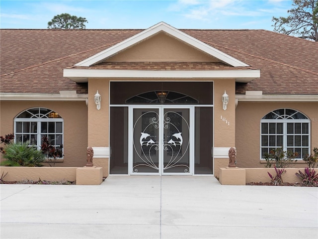 entrance to property featuring a shingled roof, concrete driveway, and stucco siding