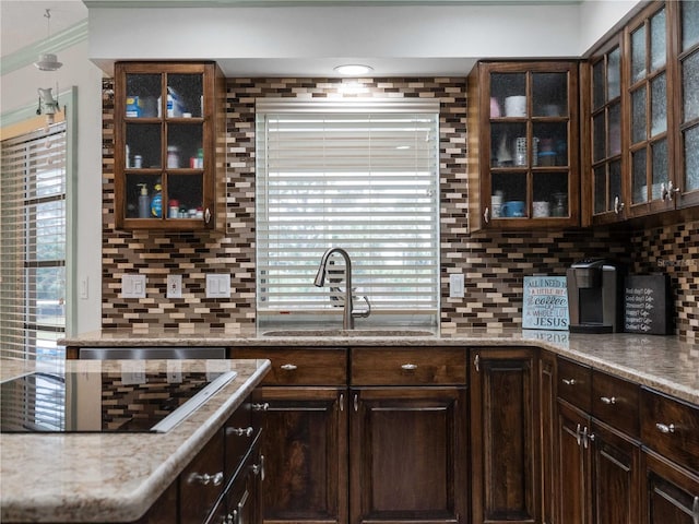 kitchen featuring black electric stovetop, a sink, dark brown cabinets, backsplash, and glass insert cabinets