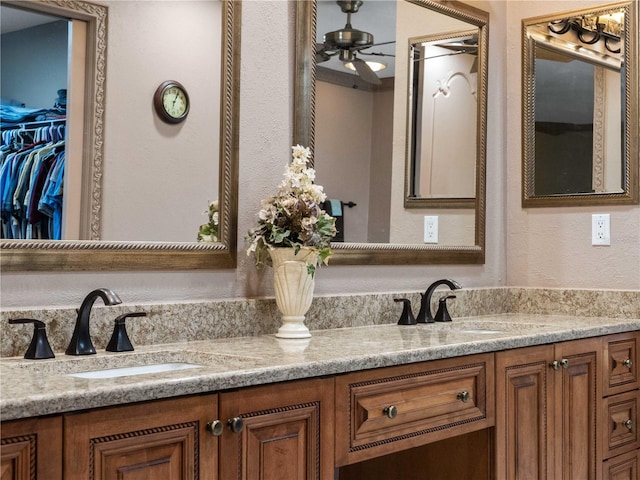 bathroom with double vanity, ceiling fan, a walk in closet, and a sink