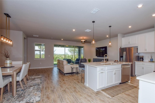 kitchen with white cabinetry, sink, hanging light fixtures, stainless steel appliances, and a center island with sink