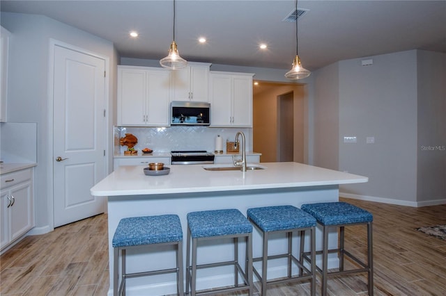 kitchen with sink, white cabinetry, stainless steel appliances, light hardwood / wood-style floors, and an island with sink