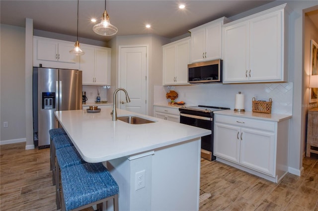 kitchen with appliances with stainless steel finishes, sink, white cabinets, a kitchen breakfast bar, and a center island with sink