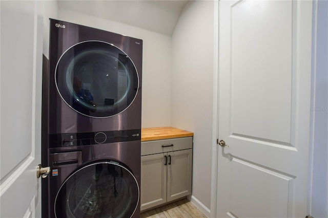 laundry room featuring stacked washer and dryer, light wood-type flooring, and cabinets