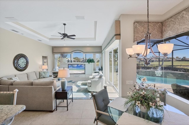 tiled dining room with a tray ceiling, ceiling fan with notable chandelier, and a healthy amount of sunlight