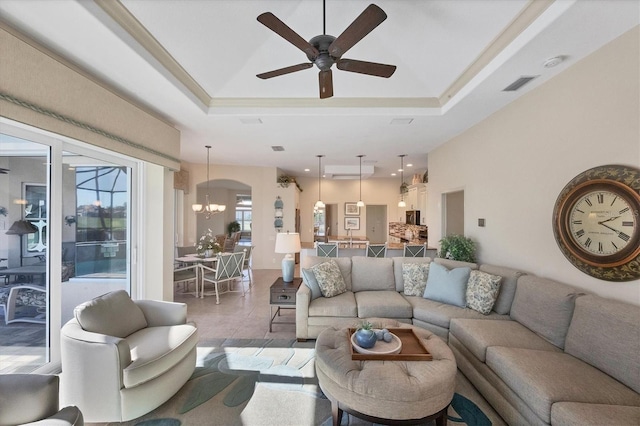 living room featuring tile patterned flooring, ceiling fan with notable chandelier, and a tray ceiling