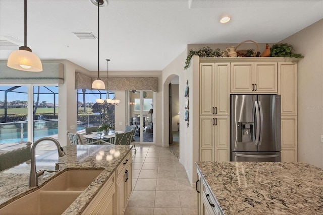 kitchen with pendant lighting, sink, light stone counters, and stainless steel refrigerator with ice dispenser