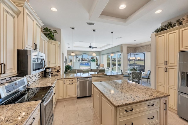 kitchen with pendant lighting, appliances with stainless steel finishes, a center island, kitchen peninsula, and a raised ceiling