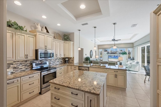 kitchen with sink, stainless steel appliances, a tray ceiling, decorative light fixtures, and kitchen peninsula