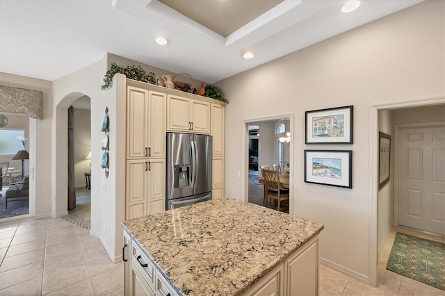 kitchen with stainless steel fridge, light stone countertops, cream cabinetry, and a center island