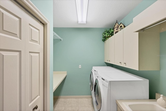 clothes washing area with washer and dryer, sink, cabinets, light tile patterned floors, and a textured ceiling