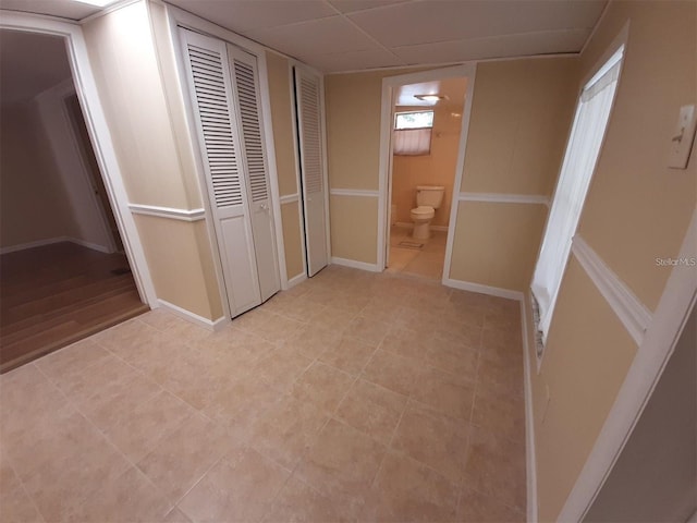 unfurnished bedroom with a paneled ceiling, light tile patterned flooring, multiple closets, and ensuite bathroom