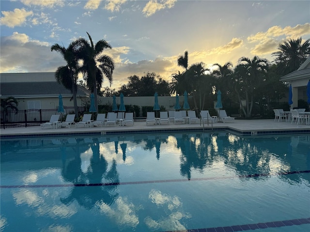 pool at dusk featuring a patio area, a community pool, and fence