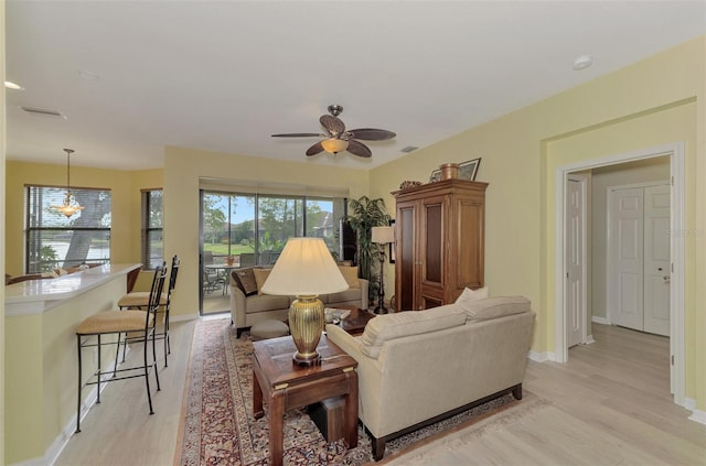 living room with ceiling fan with notable chandelier and light hardwood / wood-style floors