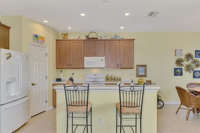 kitchen featuring a kitchen breakfast bar, a kitchen island, light tile patterned floors, and white appliances