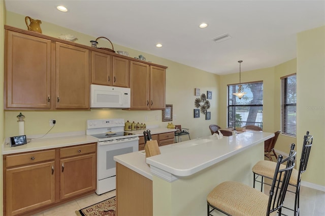 kitchen with light tile patterned flooring, a breakfast bar, hanging light fixtures, a center island with sink, and white appliances