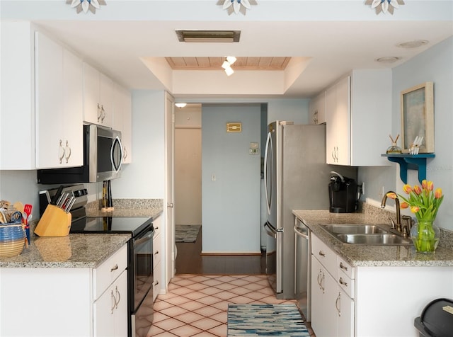 kitchen with sink, white cabinetry, light stone counters, appliances with stainless steel finishes, and a raised ceiling