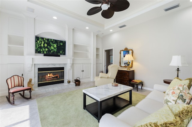 living room with crown molding, built in features, ceiling fan, a high end fireplace, and a raised ceiling