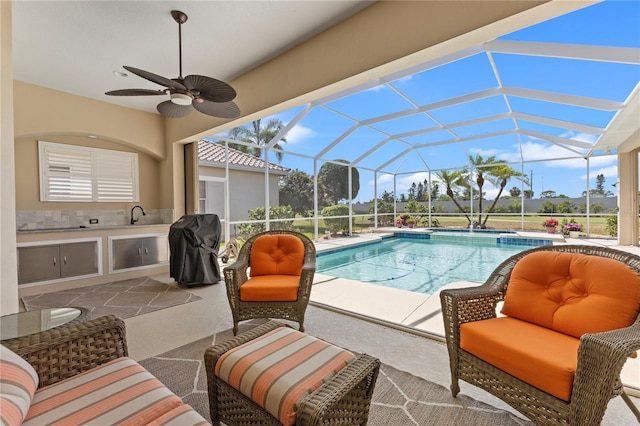 view of swimming pool featuring an outdoor kitchen, grilling area, glass enclosure, ceiling fan, and a patio