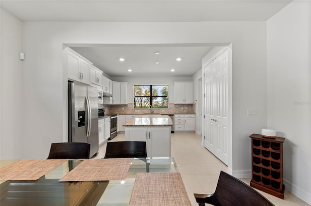 kitchen featuring a kitchen island, white cabinetry, decorative backsplash, light stone counters, and stainless steel appliances