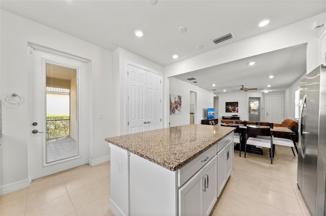 kitchen featuring light tile patterned flooring, white cabinetry, stainless steel refrigerator, a kitchen island, and light stone countertops