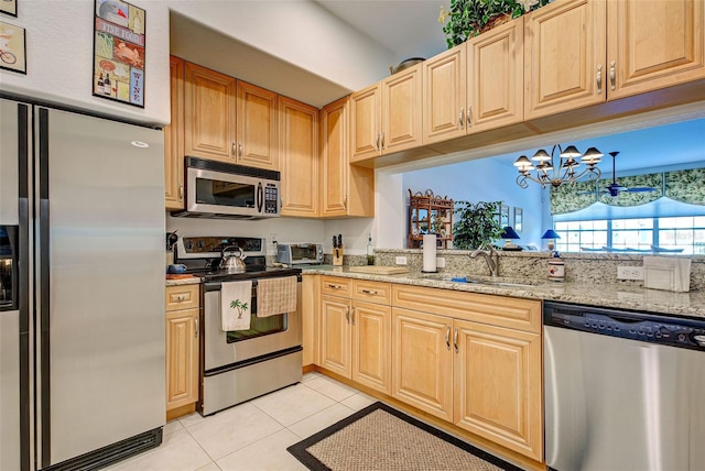 kitchen featuring sink, light stone counters, an inviting chandelier, light tile patterned floors, and stainless steel appliances