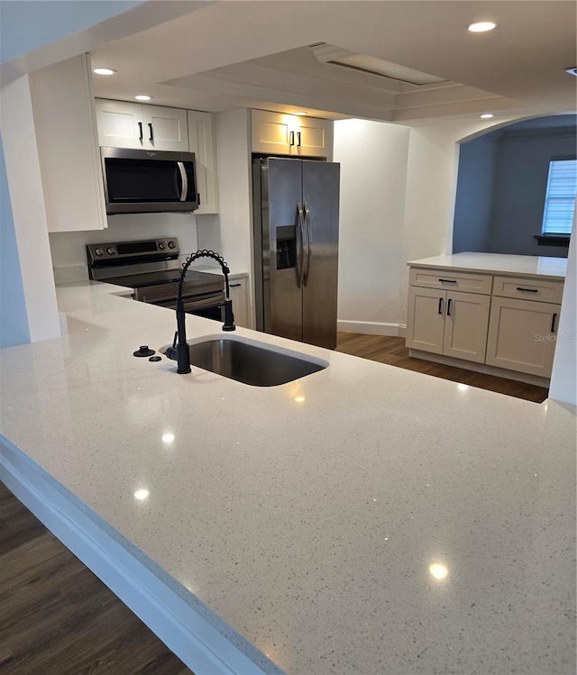 kitchen featuring dark wood-type flooring, sink, appliances with stainless steel finishes, kitchen peninsula, and white cabinets