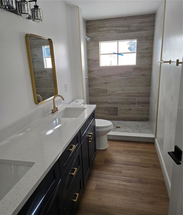 bathroom with hardwood / wood-style floors, vanity, a tile shower, and toilet