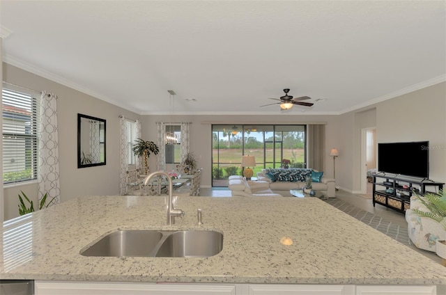 kitchen featuring light stone counters, ornamental molding, sink, and a center island with sink