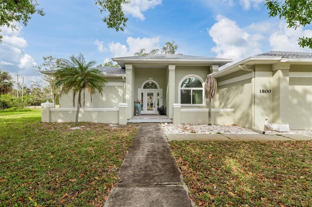 view of exterior entry featuring a yard, french doors, and stucco siding