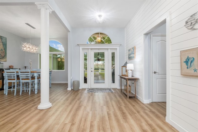 entrance foyer featuring light wood-type flooring, baseboards, ornate columns, and an inviting chandelier