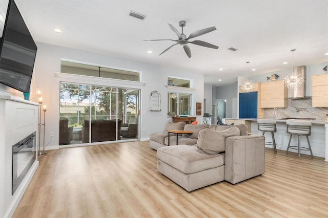 living area with recessed lighting, visible vents, a glass covered fireplace, ceiling fan, and light wood-type flooring