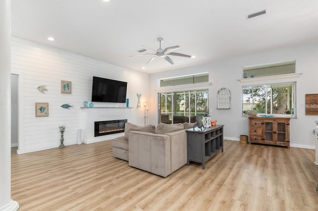 living area with a ceiling fan, baseboards, visible vents, light wood-style floors, and a glass covered fireplace